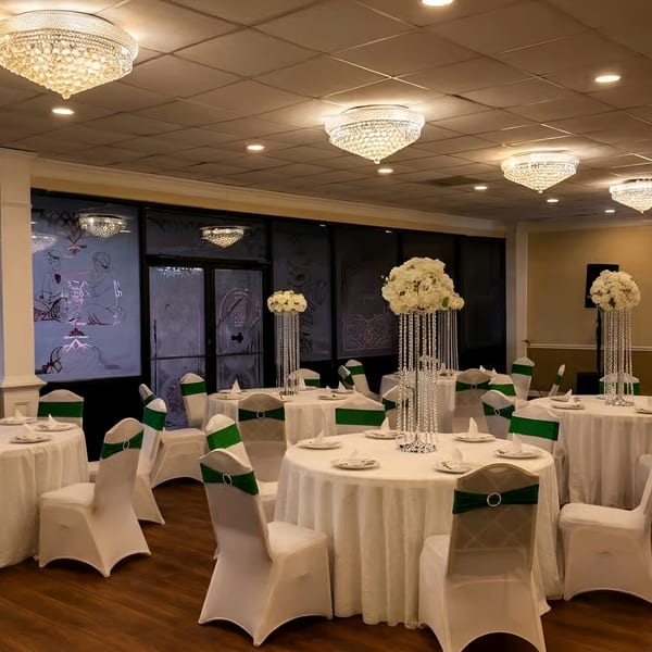 Elegant dining room with round tables, white tablecloths, green chair sashes, and crystal chandeliers.