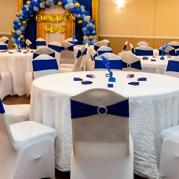 A banquet hall set for a graduation party with round tables, white tablecloths, and blue chair sashes.
