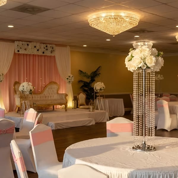 Elegant event hall with white tables, pink chairs, and a stage with a gold sofa.