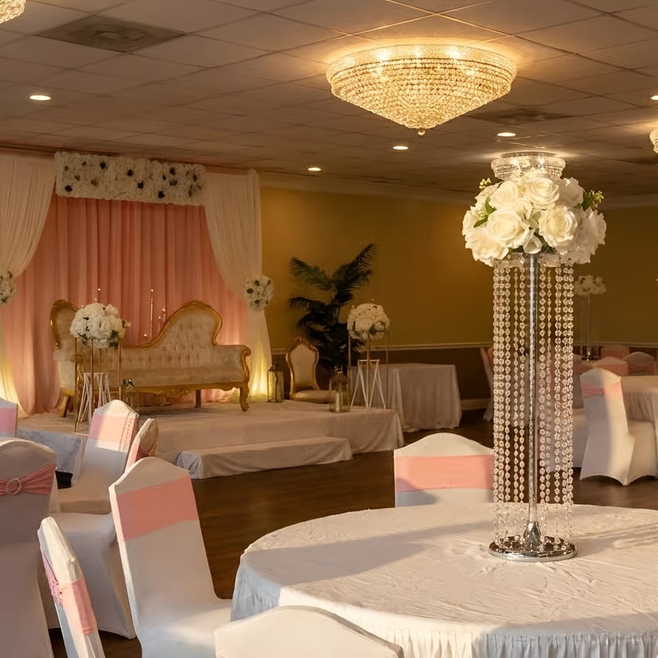 Elegant event hall with white tables, pink chairs, and a stage with a gold sofa.