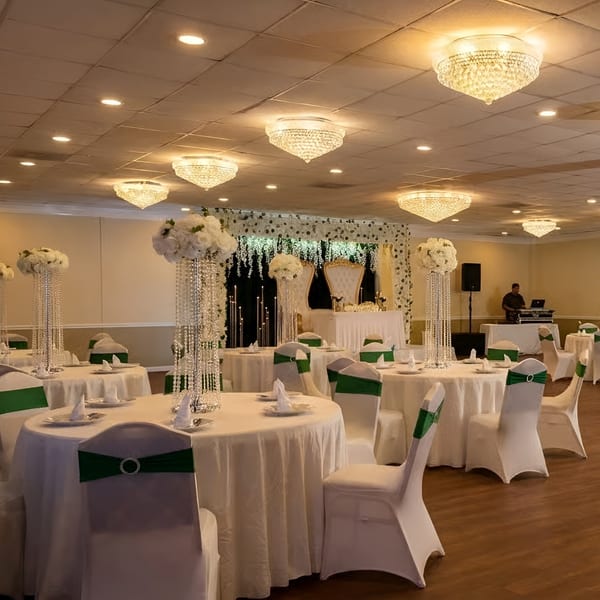 Elegant banquet hall with round tables, white tablecloths, green chair sashes, and floral centerpieces.