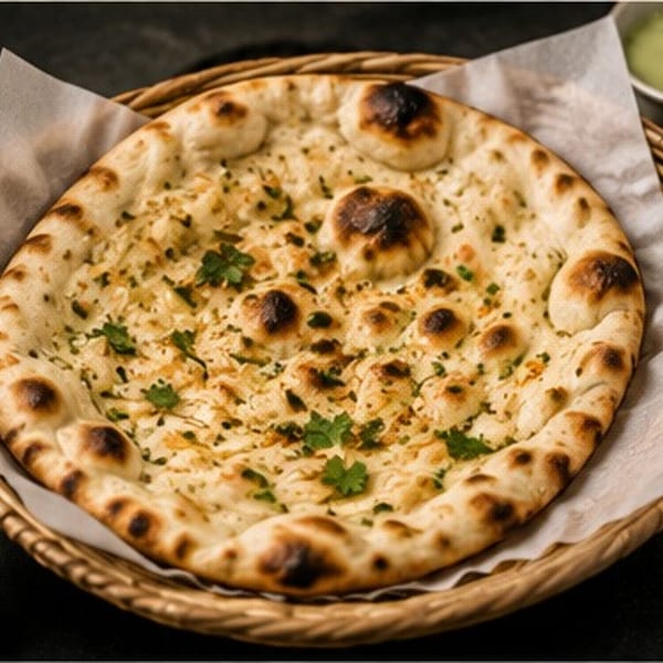 Garlic naan bread in a woven basket with green chutney and chili flakes on the side.